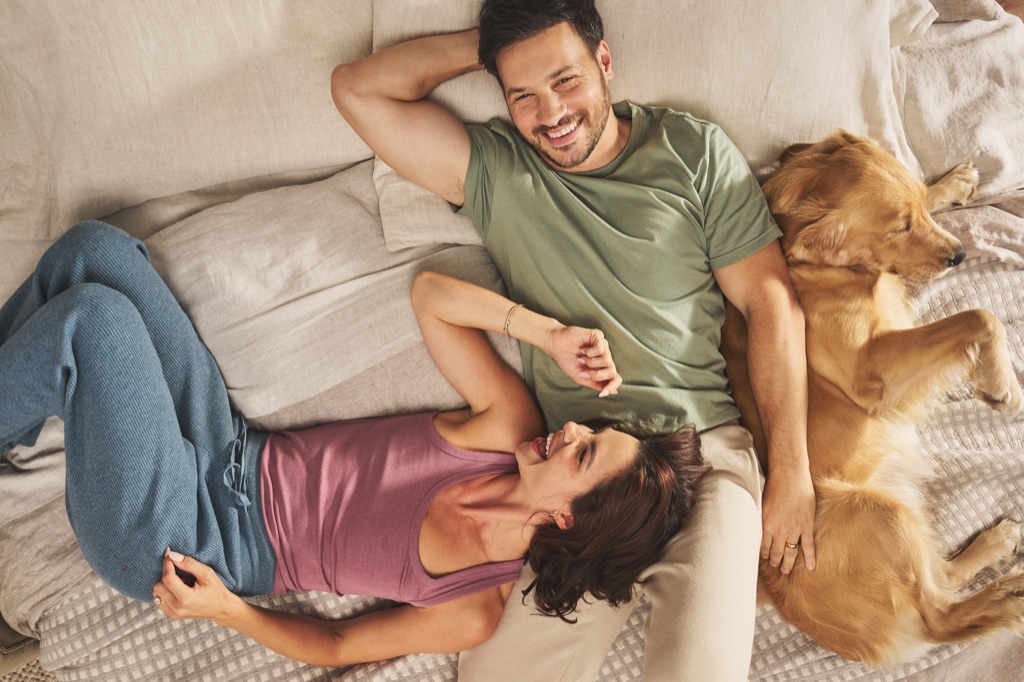Couple lying back on a bed laughing with a golden retriever asleep beside them