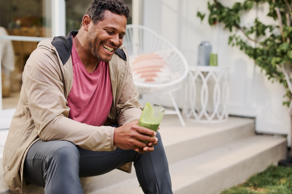 Man laughing with a green smoothie on his back porch steps