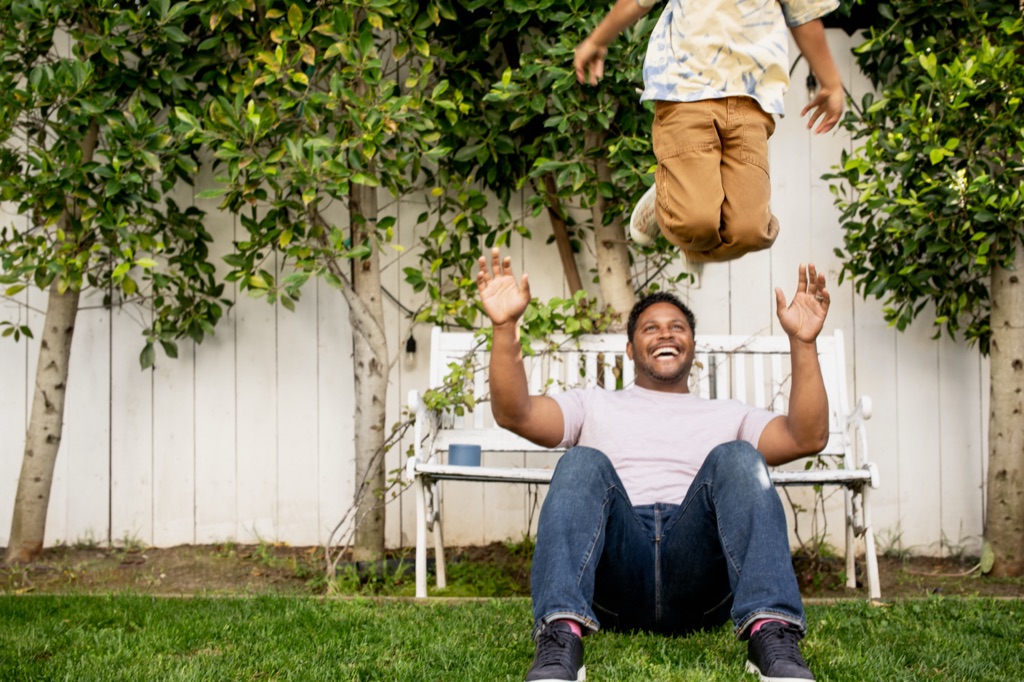 Dad on the grass tossing his young child high in the air in a backyard