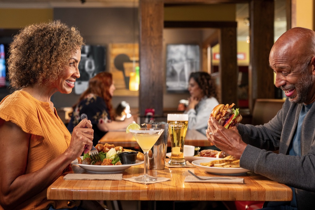 Date night couple at a pub table with a burger, salad, and margarita