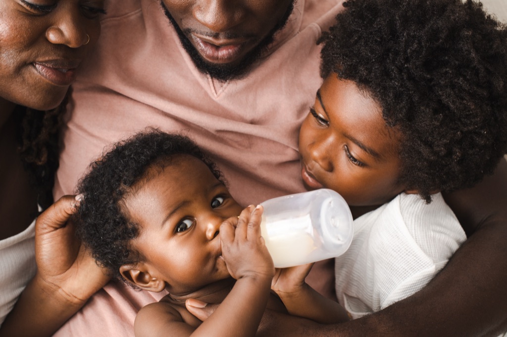 Close overhead of parents and a big brother watching the baby drink from a bottle