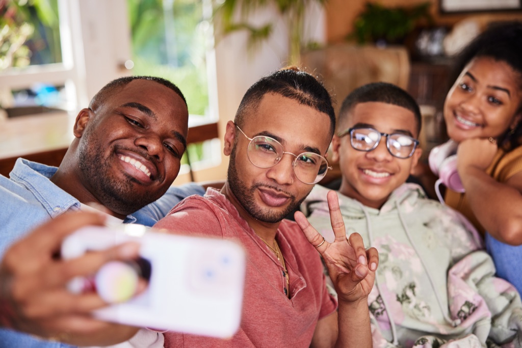 Dad taking a selfie with his family on the couch while a teen flashes a peace sign