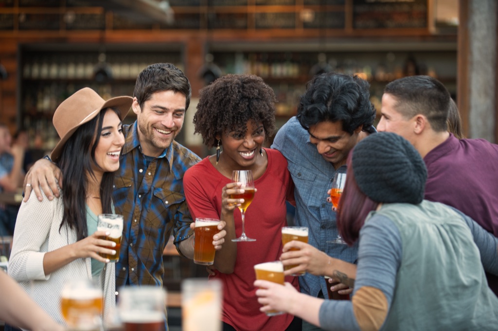 Six friends laughing and toasting with craft beers and cocktails at an outdoor brewery bar