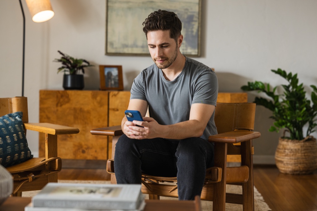 Man in a leather safari chair reading his phone in a midcentury living room
