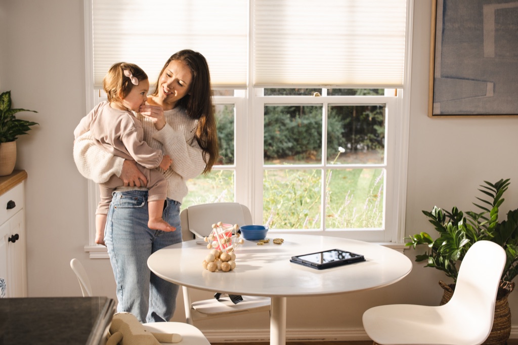 Mom holding her toddler in a sunny breakfast nook with a tablet on the table