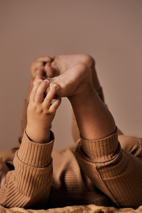 Baby in a camel ribbed set lying back holding its own bare feet