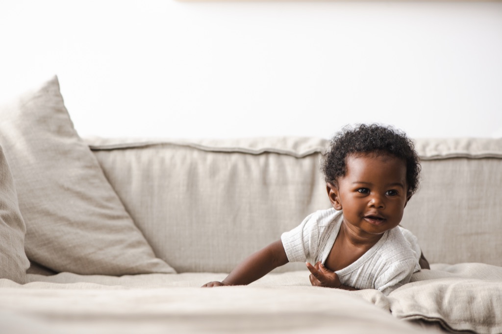 Smiling baby crawling across a beige linen couch