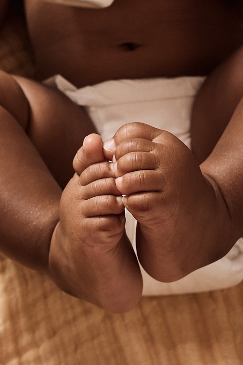 Closeup of crossed baby foot soles in a diaper on ochre muslin