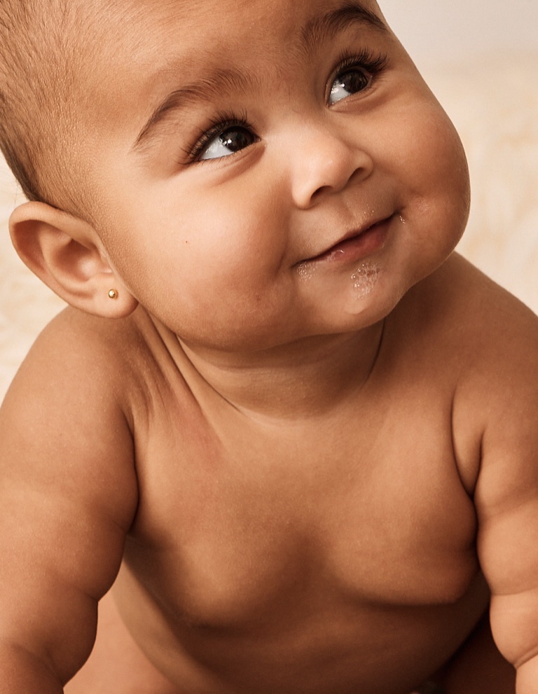 Baby with a tiny gold stud earring looking up with milk bubbles on its lips
