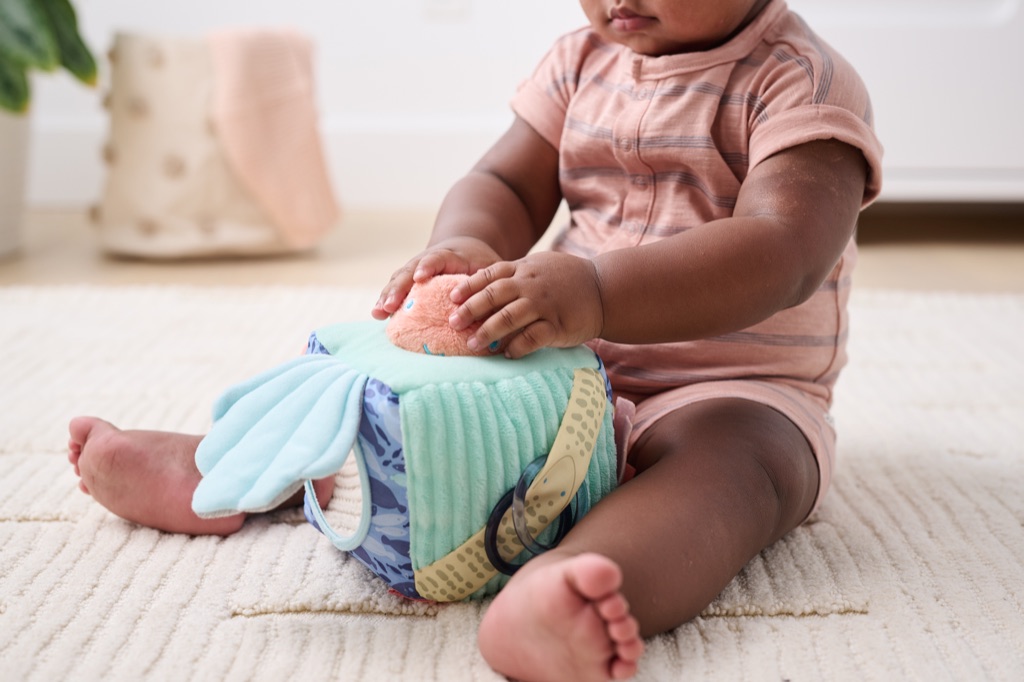 Baby in a striped romper exploring an ocean themed soft sensory cube