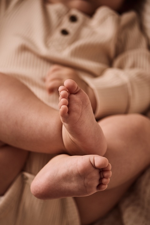 Closeup of crossed baby feet in a beige ribbed button romper
