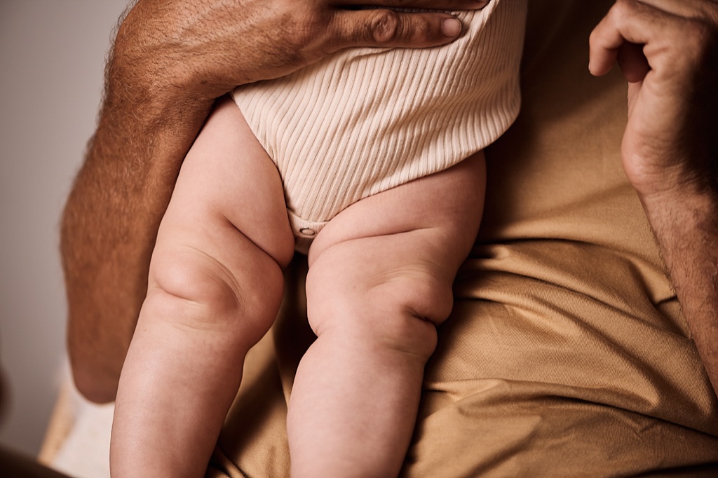 Dad's arms holding his baby with chubby crossed legs