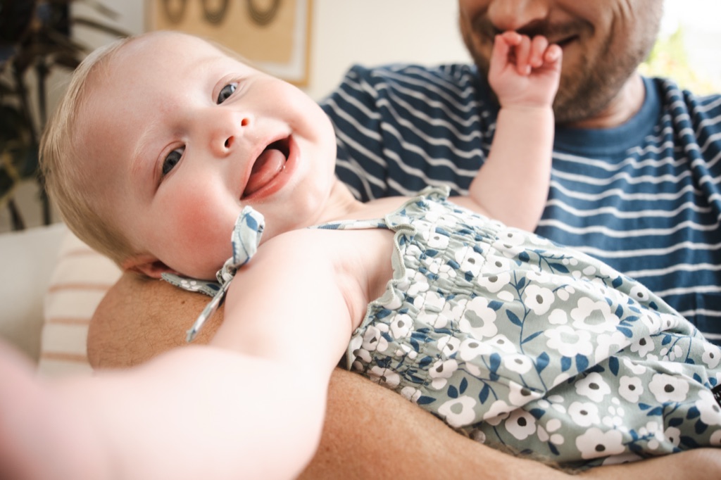 Dad in a navy striped tee holding his laughing baby in a floral romper close