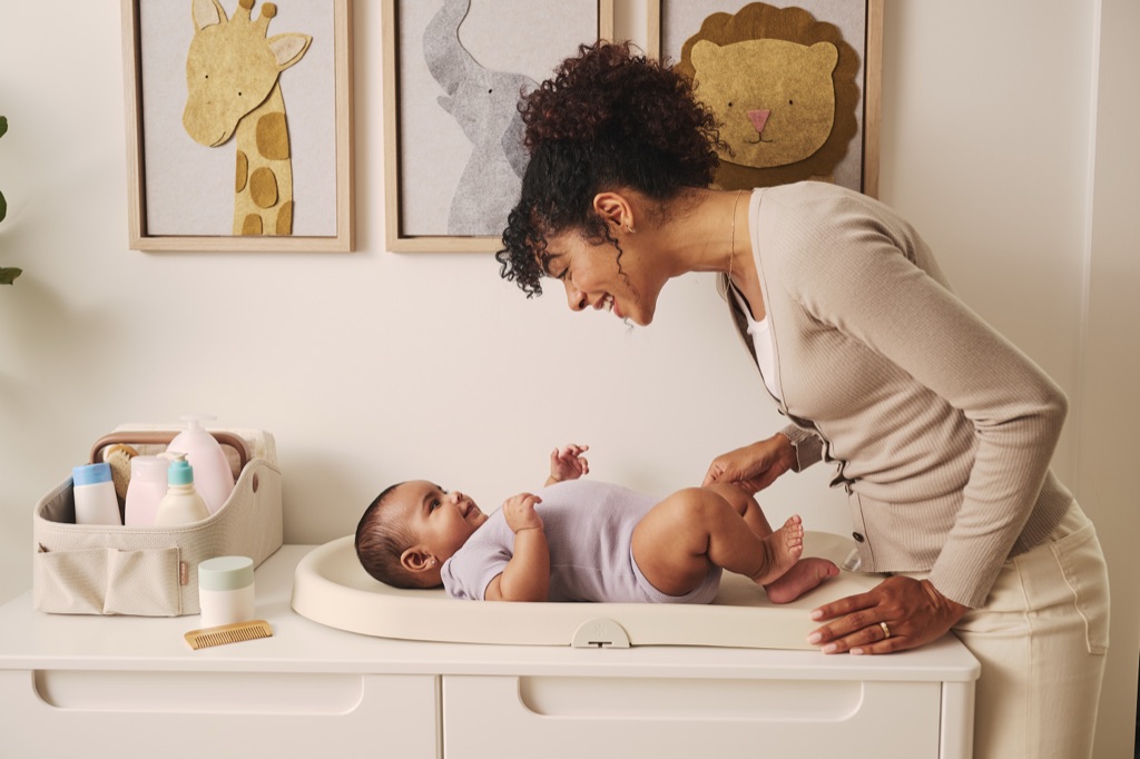 Mom smiling over her baby on a changing pad beneath felt giraffe, elephant, and lion nursery art
