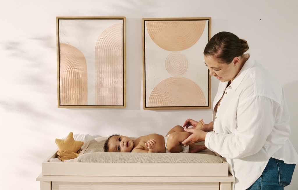 Mom changing her baby's diaper on a changing table beneath textured blush artwork