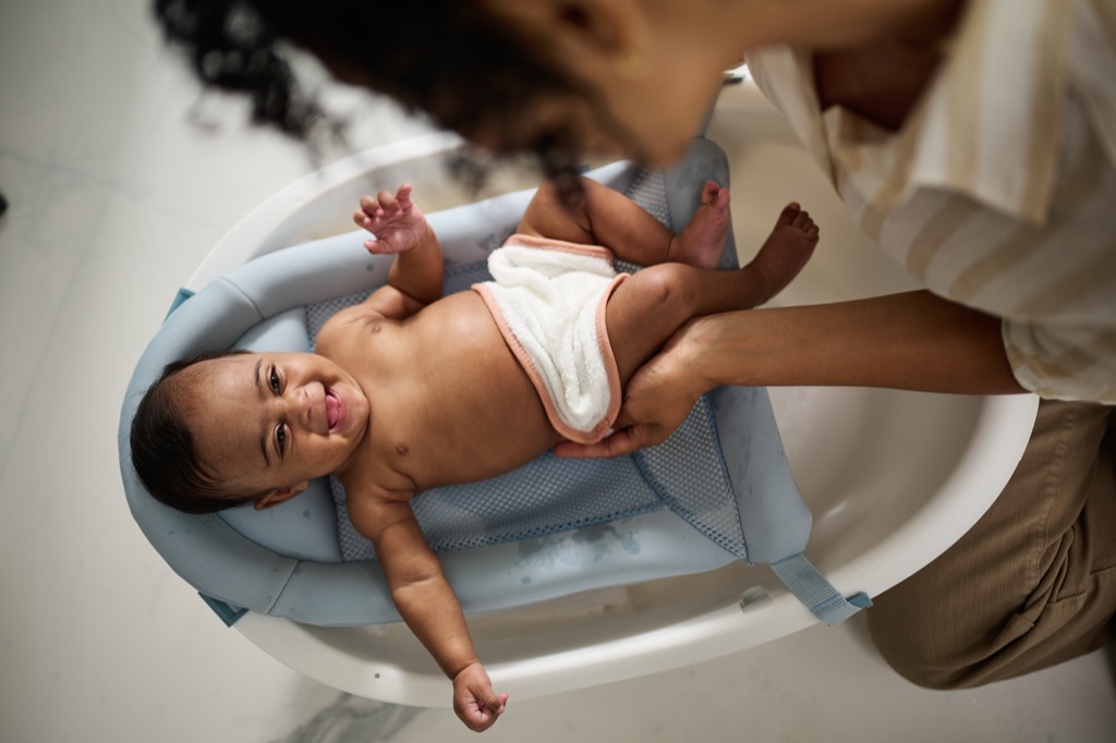 Overhead view of a smiling newborn in a baby bath supported by a parent's hands
