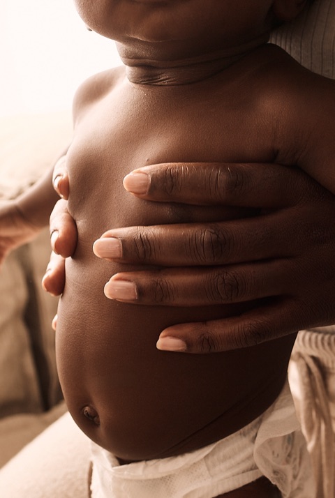 Backlit closeup of a parent's hand held gently across a baby's bare tummy