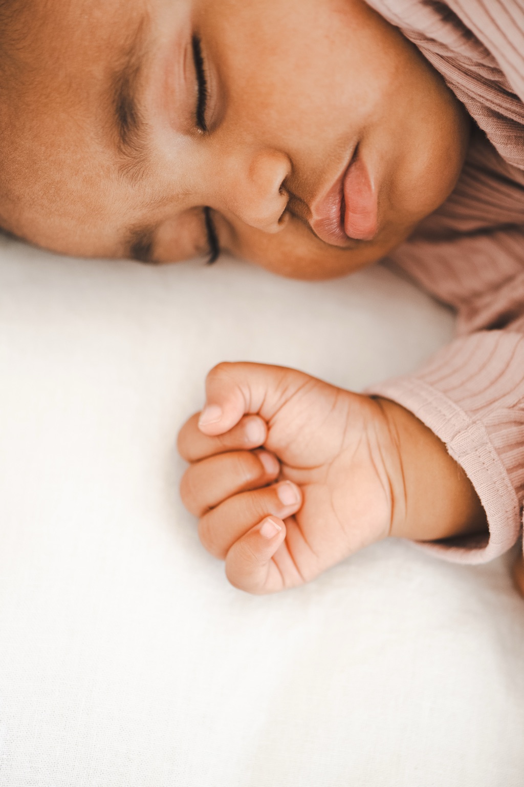 Closeup of a sleeping baby's face and tiny fist in a blush ribbed top