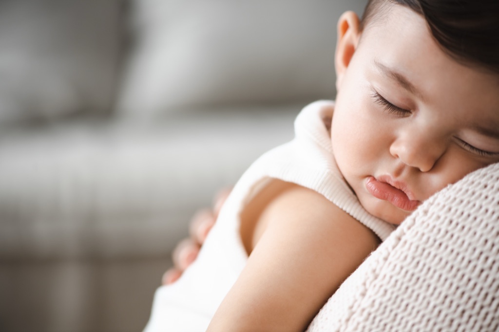 Sleeping toddler resting its head on a parent's shoulder, photographed by Dawn Heumann