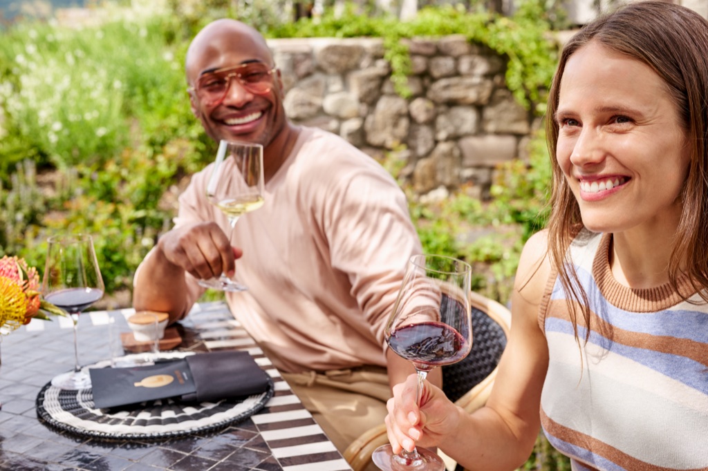Couple mid-laugh over red and white pours at a stone-walled Napa Valley garden terrace