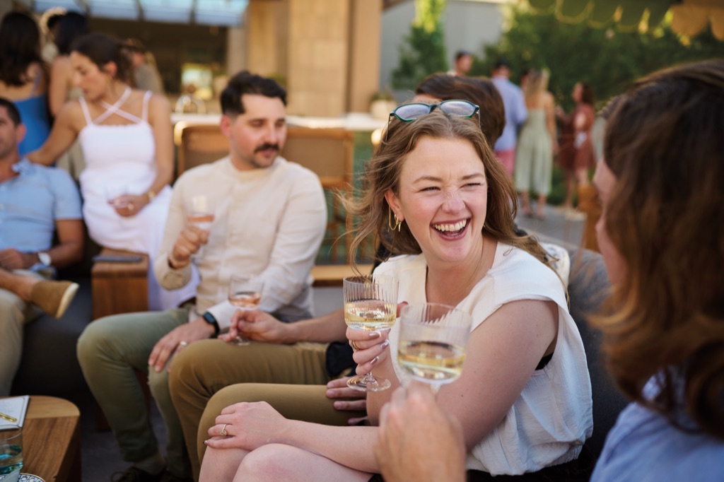 Woman laughing with white wine among friends at a Napa Valley winery terrace party