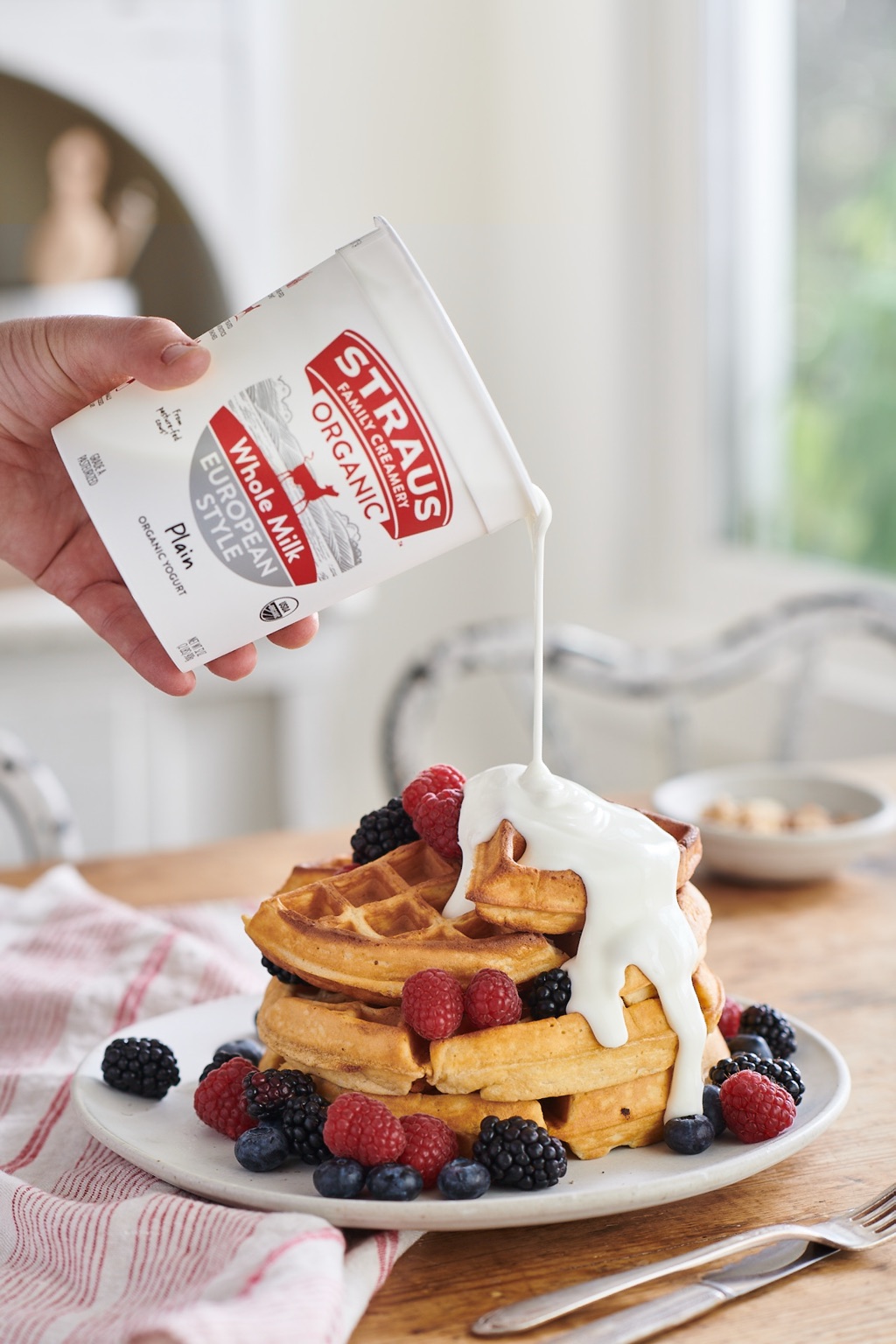 Straus European Style yogurt pouring over a waffle stack with berries