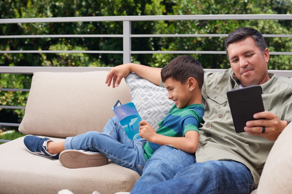 Father and son reading their Kindles together on an outdoor patio sofa, Amazon Kindle campaign