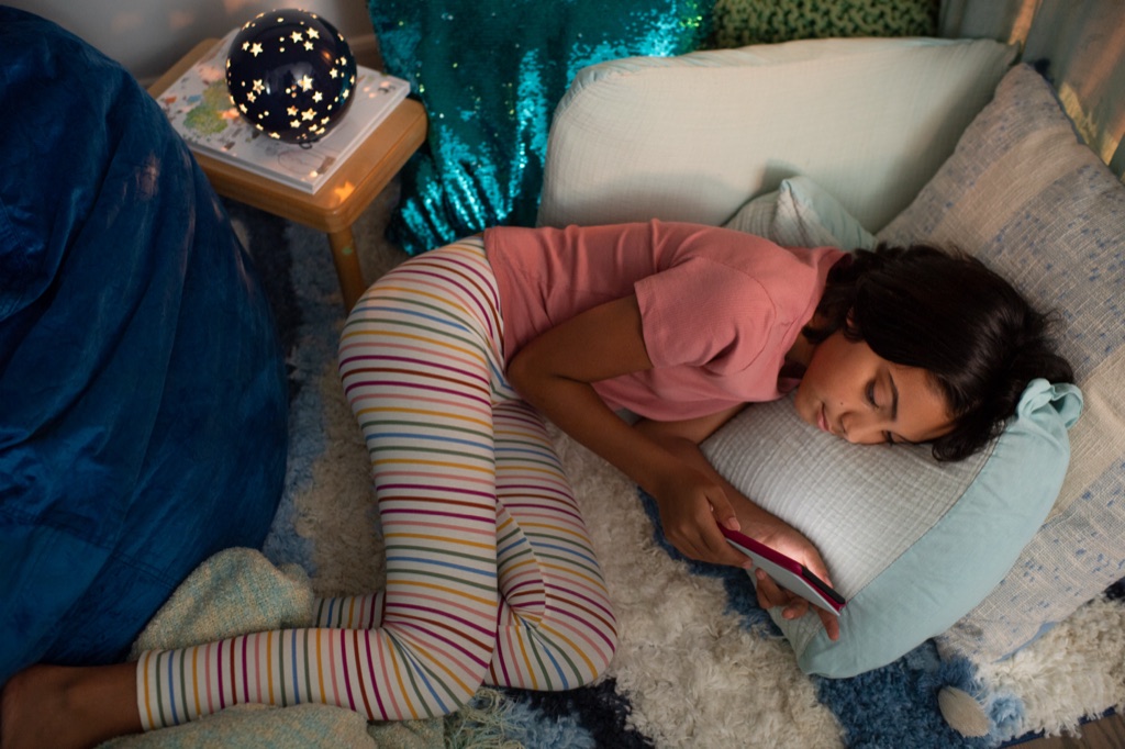 Girl fallen asleep with her Kindle beside a star projector lamp, Amazon Kindle bedtime campaign
