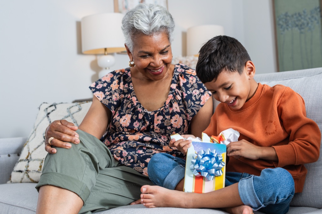 Grandmother smiling as her grandson unwraps a Kindle gift on the couch, Amazon lifestyle photography
