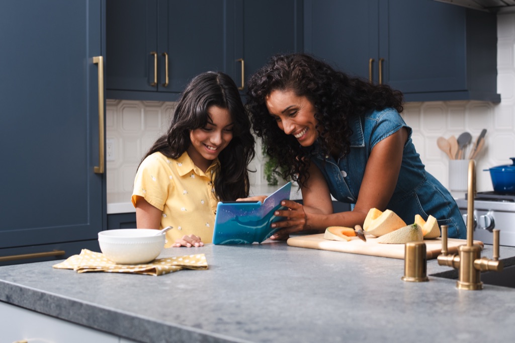 Mother and daughter laughing over a Kindle Kids e-reader at the kitchen counter, Amazon campaign