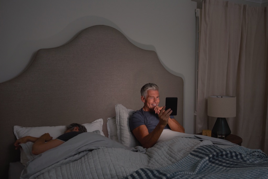 Man reading his Kindle in bed at night while his partner sleeps, Amazon Kindle campaign photography