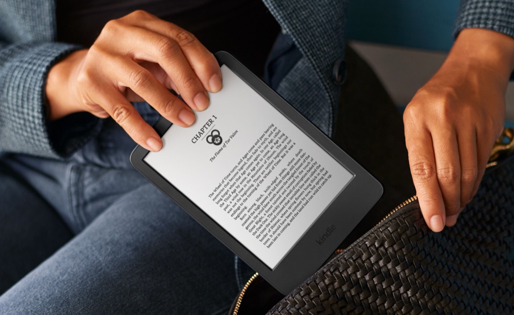 Hands slipping a Kindle into a woven leather bag, Amazon Kindle product lifestyle detail