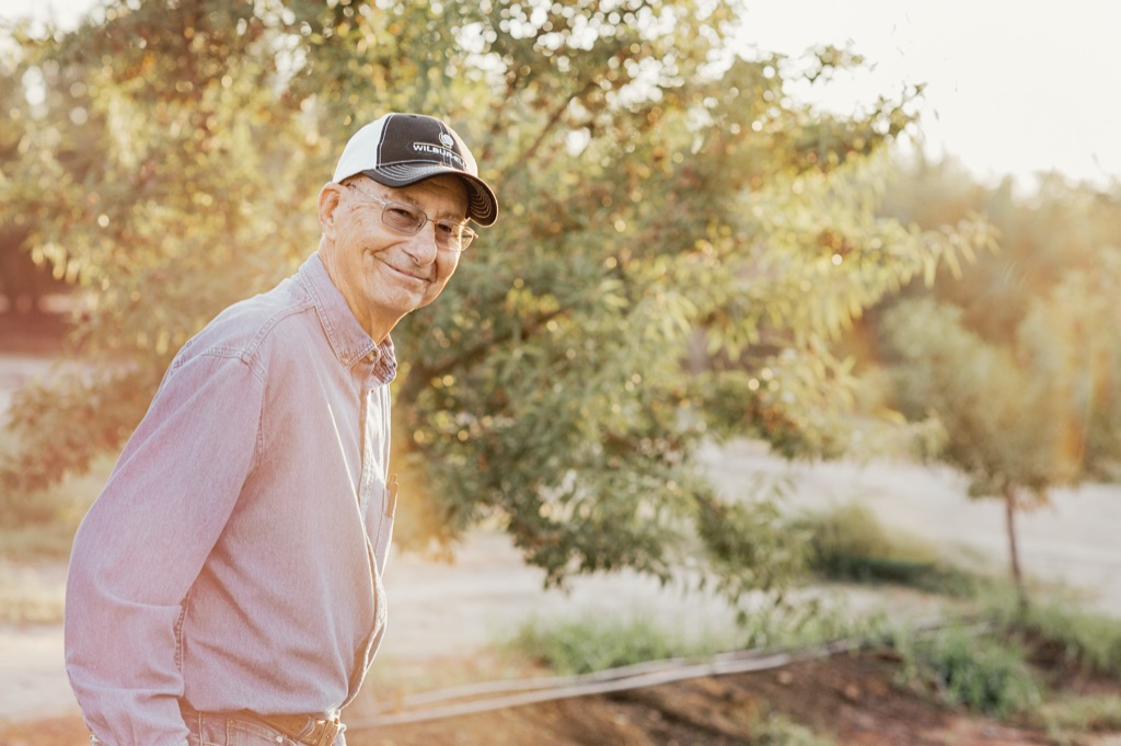 Almond farmer in a cap and denim shirt smiling in his orchard at golden hour
