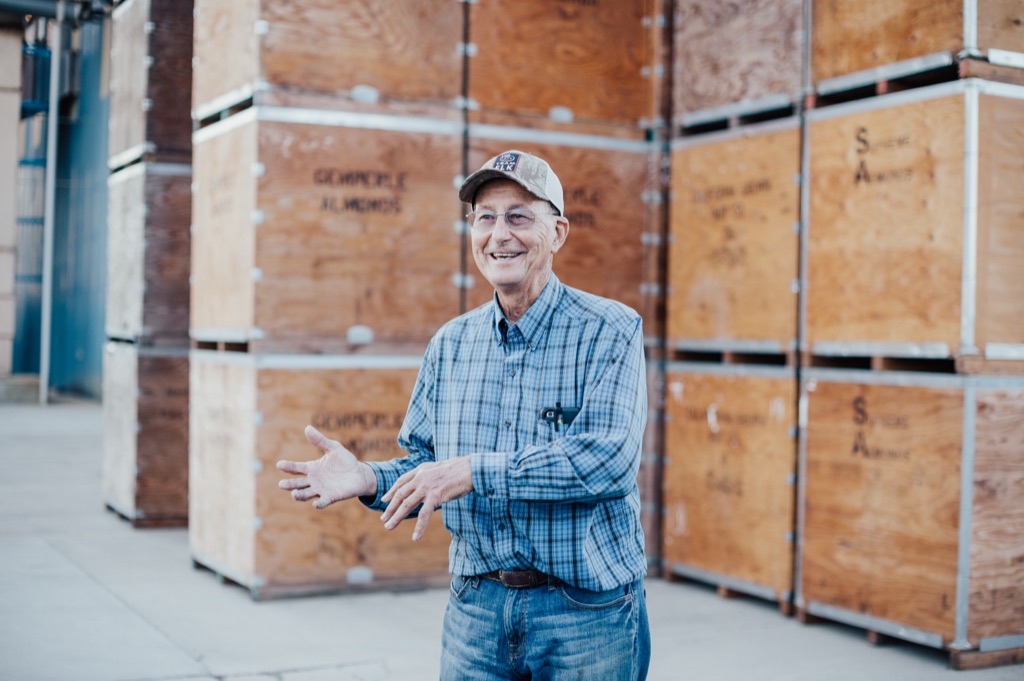 Almond grower laughing in front of stacked plywood almond bins at the huller