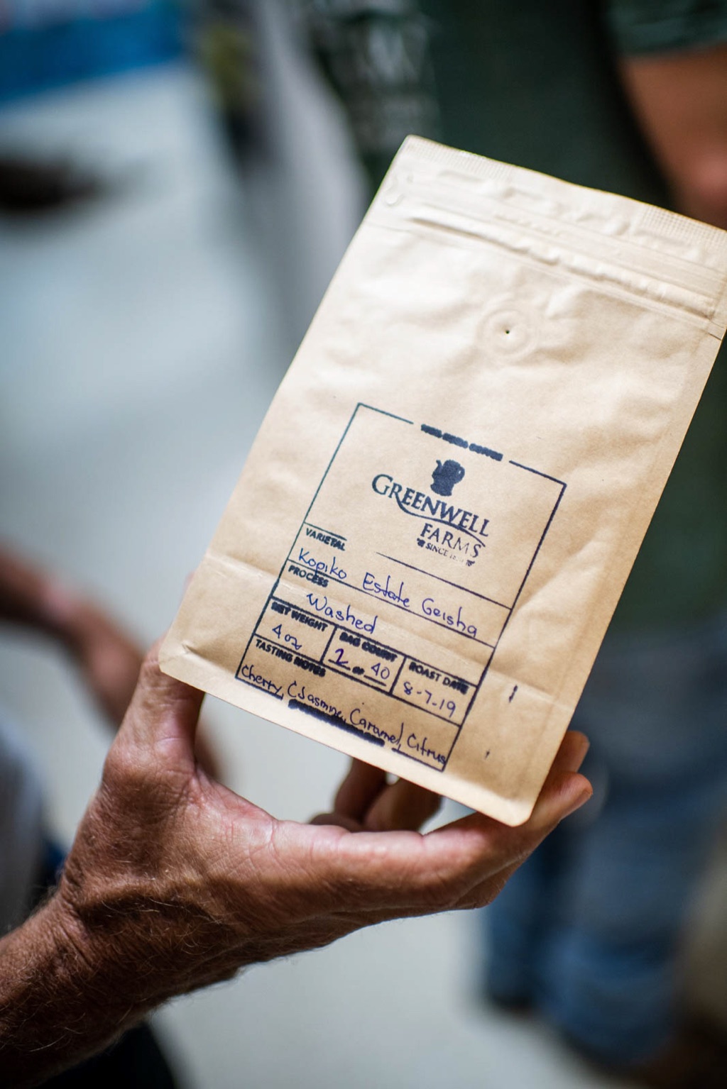 Hand holding a Greenwell Farms Kona coffee bag stamped with varietal and tasting notes