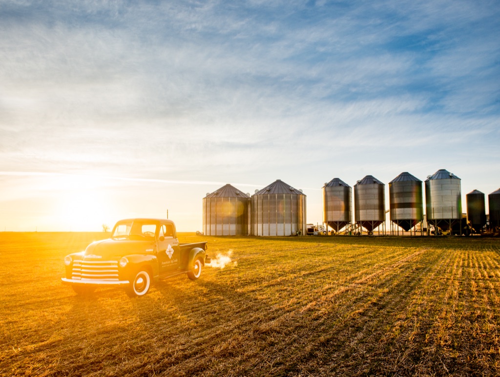 Vintage pickup truck with the American AgCredit logo parked before a line of grain silos at sunrise