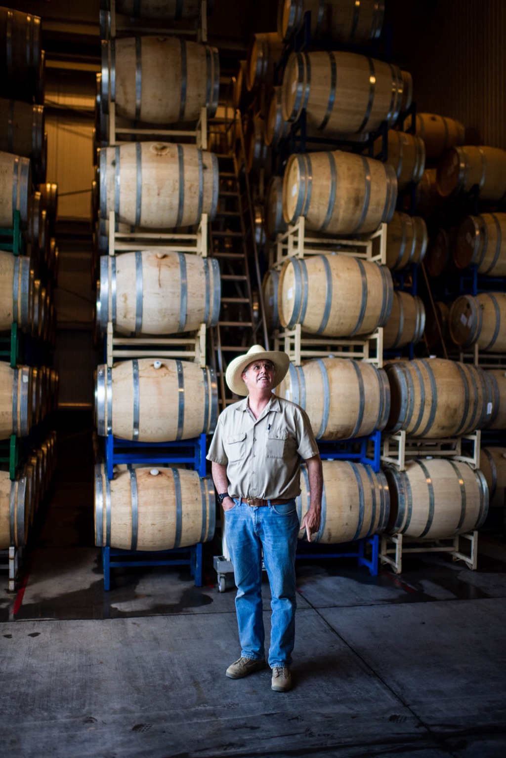 Winemaker in a straw hat standing among stacked oak wine barrels