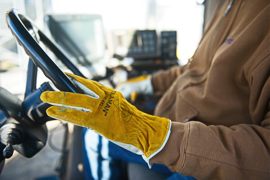 Yellow Tillman work glove resting on a tractor steering wheel with cab monitors behind