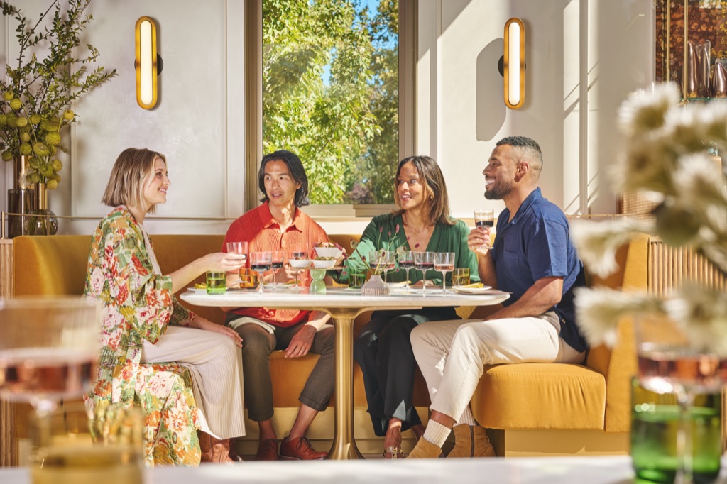 Four friends toasting glasses of red wine in a mustard banquette by the window at Bella Union winery in Napa Valley