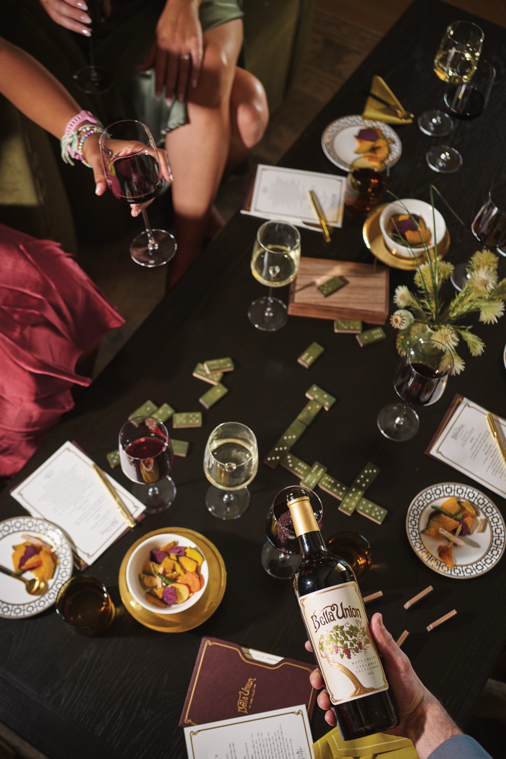 Hand holding a bottle of Bella Union Napa Valley Cabernet Sauvignon over a domino game table, photographed by Dawn Heumann