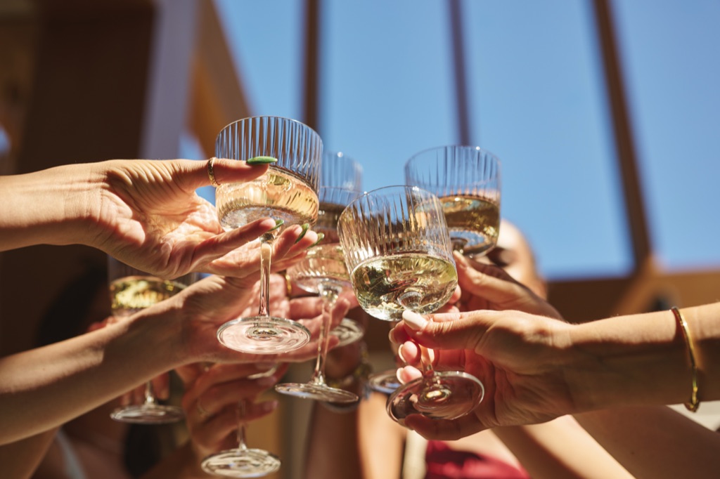 Low angle of friends clinking ribbed glasses of white wine against a clear blue sky