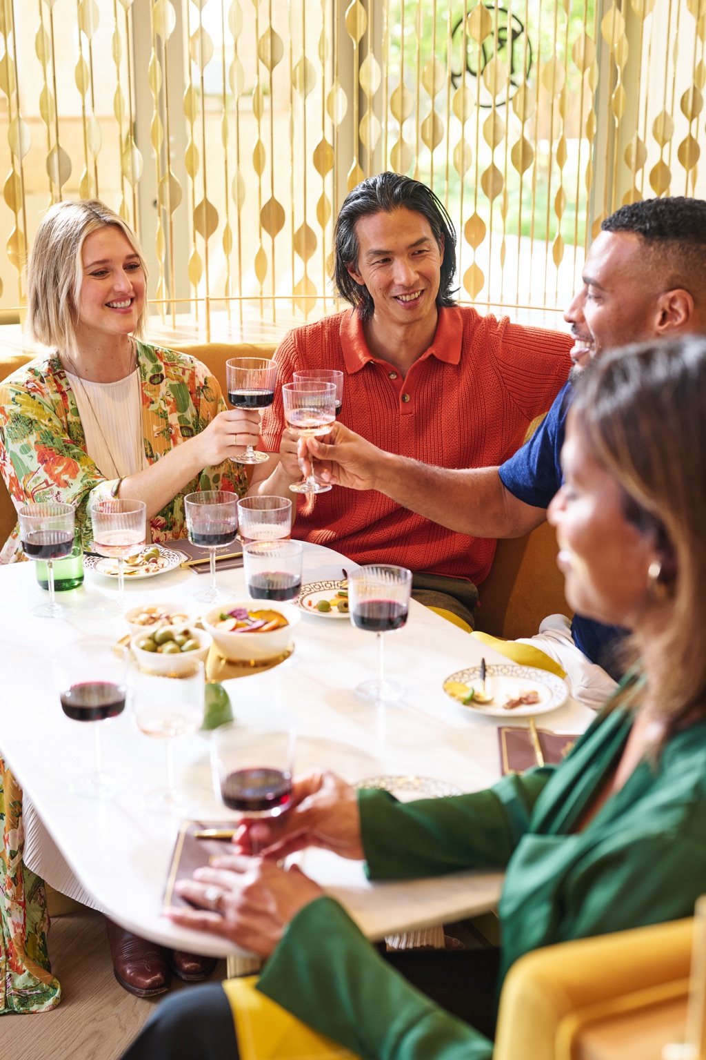 Group clinking glasses of red and rose wine at a table behind a gold kinetic bead screen