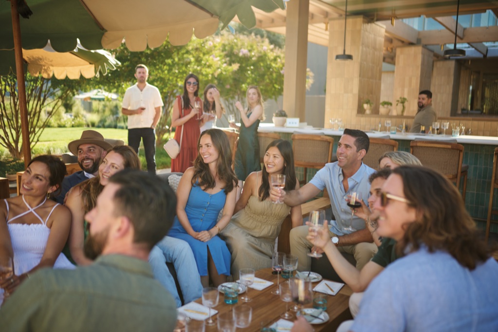 Friends raising glasses of wine together under scalloped umbrellas on the sunny winery patio