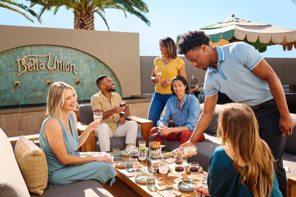 Server pouring Bella Union white wine for friends in the patio lounge beside the teal-tiled Bella Union fountain wall, photographed by Dawn Heumann