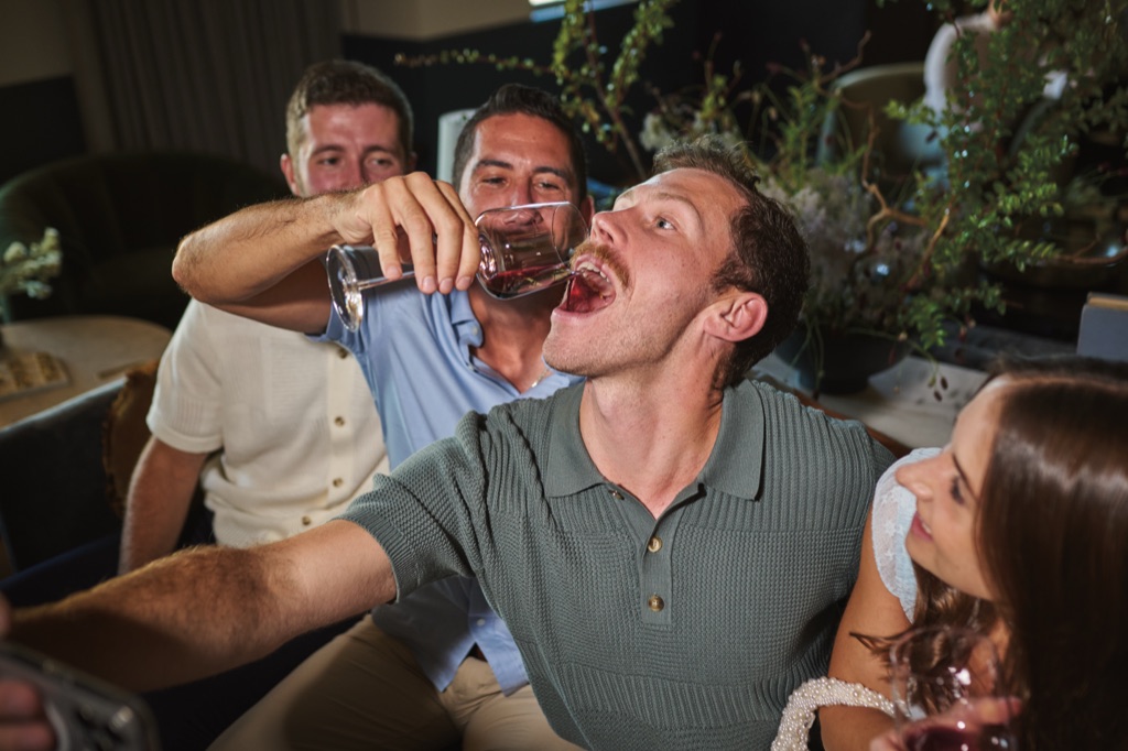 Playful moment of a man pouring wine into his friend's mouth in the winery lounge