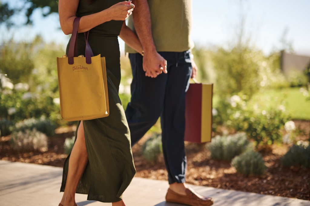 Close-up of the Bella Union paper wine tote and two-bottle gift box carried by a couple holding hands