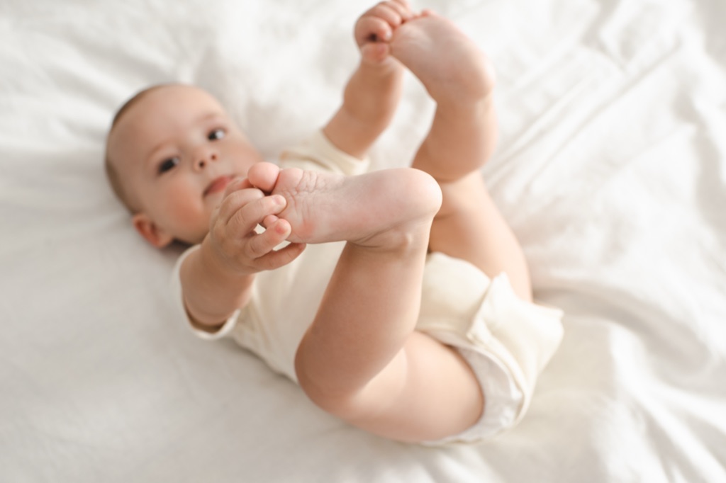 Baby lying on a white bed grabbing their toes, photographed for ByHeart