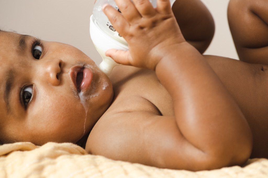 Close-up of a baby holding a bottle to their mouth with a trail of milk on their cheek, ByHeart photography