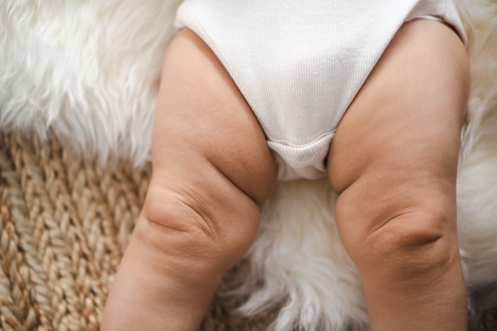 Detail of a baby's chubby legs in a white bodysuit on a sheepskin rug