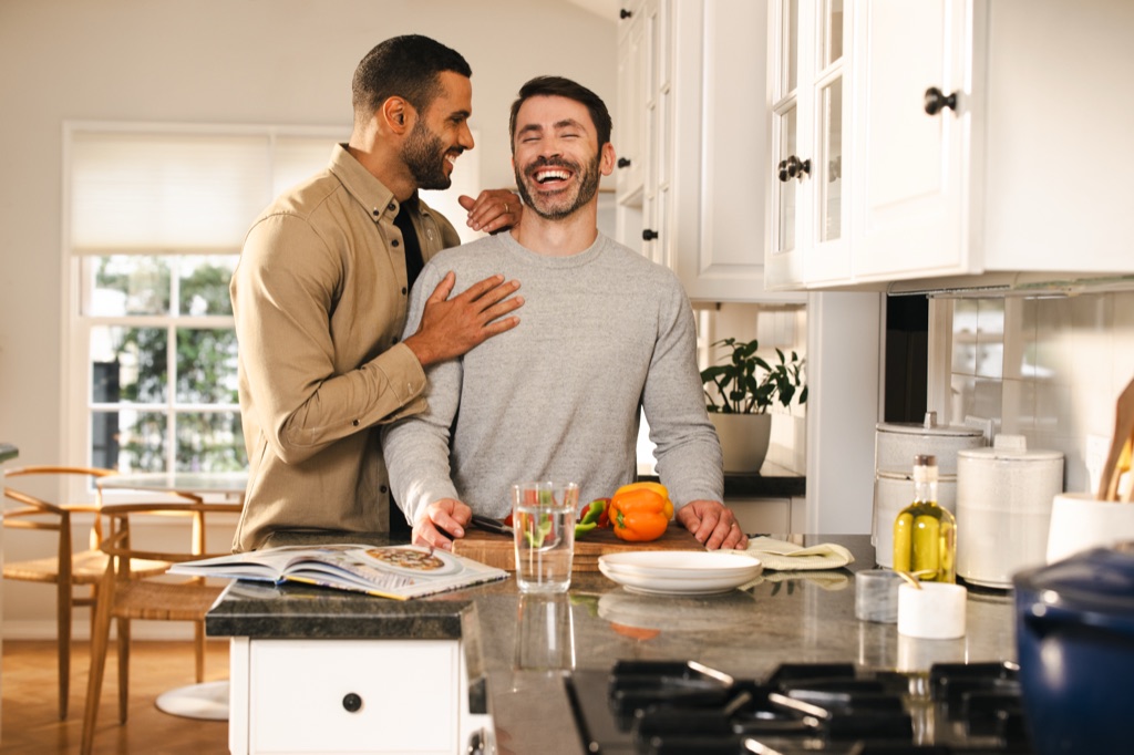 Two men laughing together while preparing vegetables in a bright white kitchen